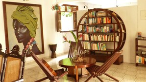 Una habitación con una estantería redonda de madera, un sillón con cojín verde, una mesa de madera y un cuadro grande con marco.