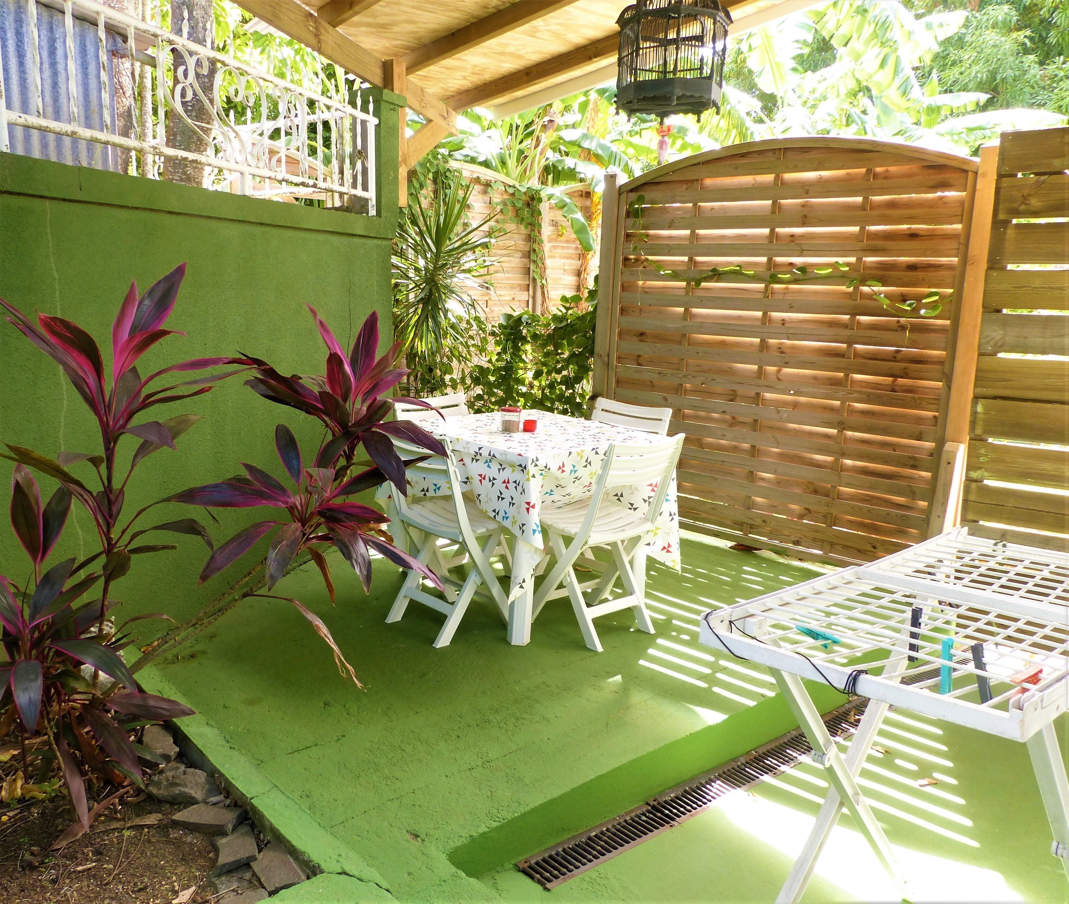 A patio area with a table and chairs, surrounded by green walls and plants.