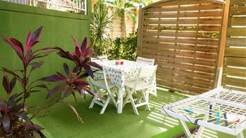 A patio area with a table and chairs, surrounded by green walls and plants.