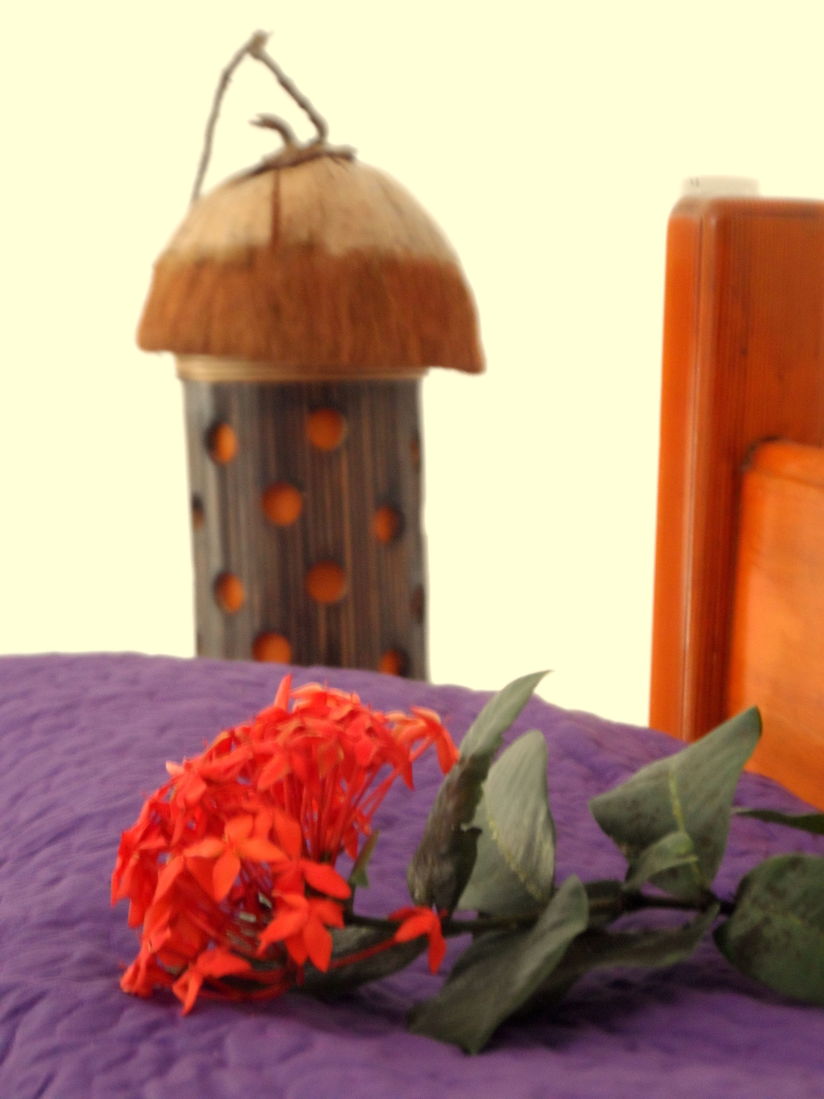 A wooden lantern with a thatched roof and orange spots, a purple cloth, and green leaves on a surface.