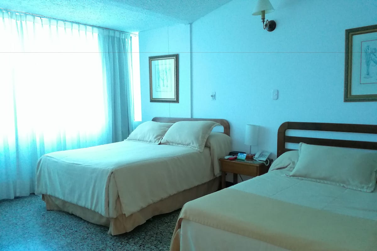 A hotel room with two beds, a nightstand with a lamp, a framed picture on the wall, and a window with curtains.