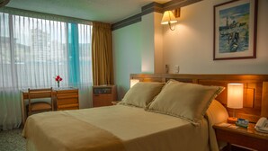 A hotel room with a large bed, a desk with a chair, a lamp, and a painting on the wall.