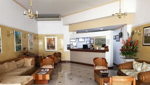 A hotel lobby with a reception desk, seating area with sofas and chairs, and a tiled floor.