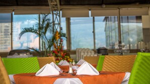 A dining table set with white napkins, silverware, and a salt shaker, surrounded by wicker chairs with green cushions.