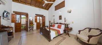A spacious bedroom with a large bed, a wooden ceiling, a wooden chair, and a desk with a computer.