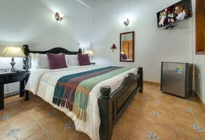 A hotel room with a bed, bedside tables, a TV, and a refrigerator.
