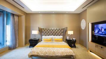 A spacious bedroom with a large bed, two bedside tables with lamps, a television, and a large window with curtains.