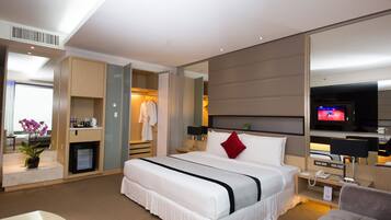 Una habitación de hotel moderna con una cama grande, televisión, escritorio con silla, espejo y una planta pequeña.