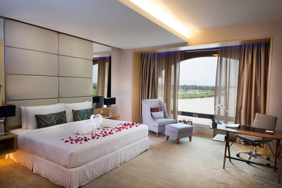A hotel room with a large bed, a desk, a chair, and a view of a body of water.