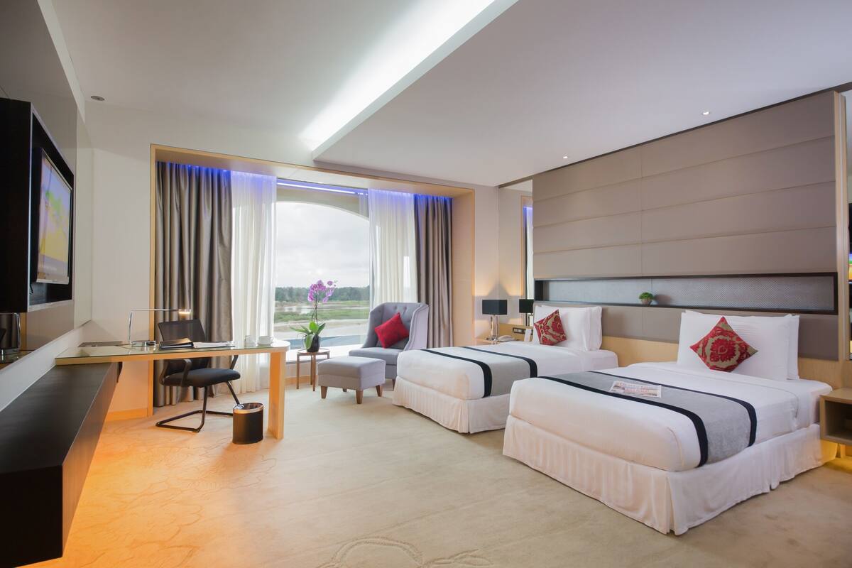 A modern hotel room with a desk, two beds, a TV, and a large window with curtains.