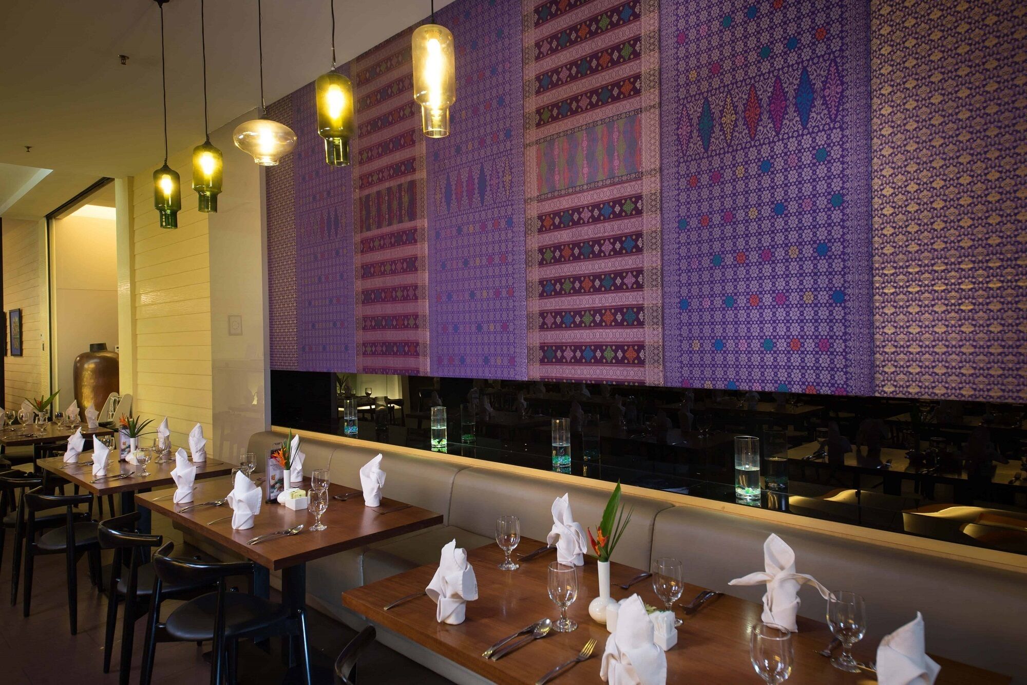 A restaurant with tables set for dining, a patterned wall, and hanging pendant lights.
