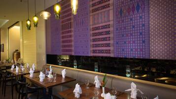 A restaurant with tables set for dining, a patterned wall, and hanging pendant lights.