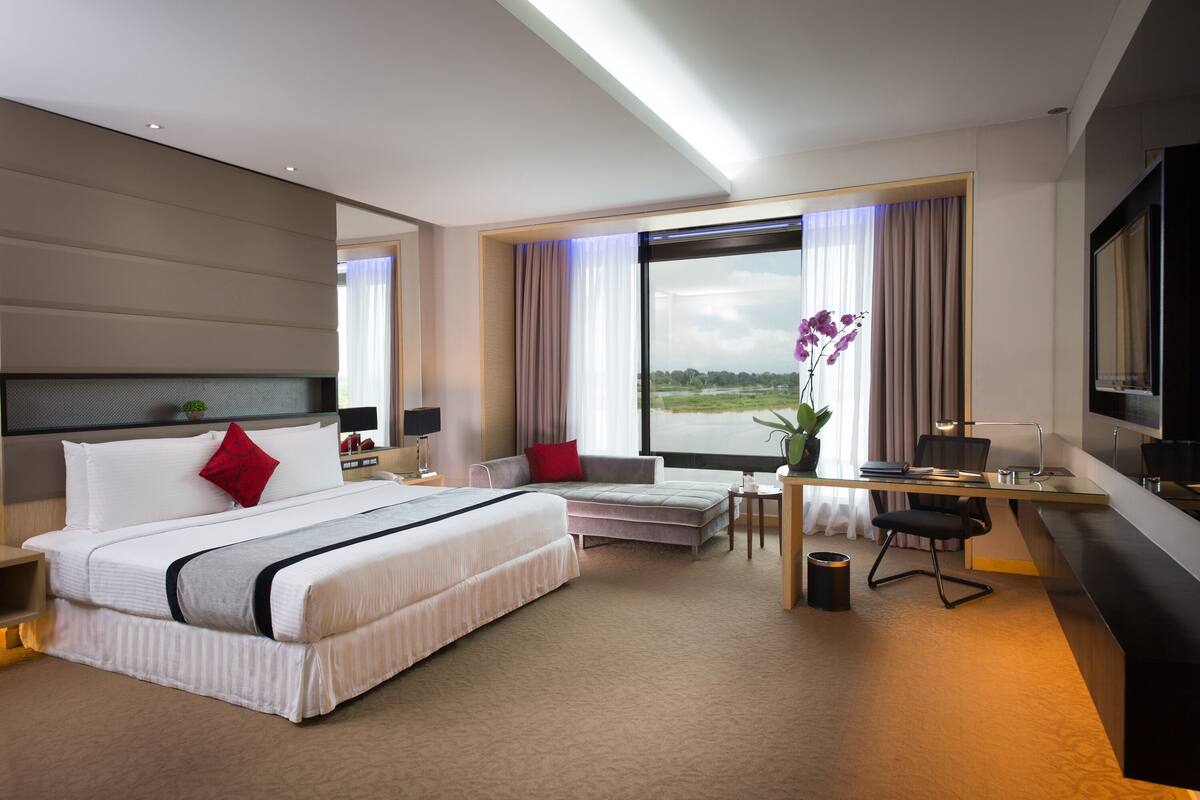 A modern hotel room with a large bed, a desk, and a view of the outdoors.