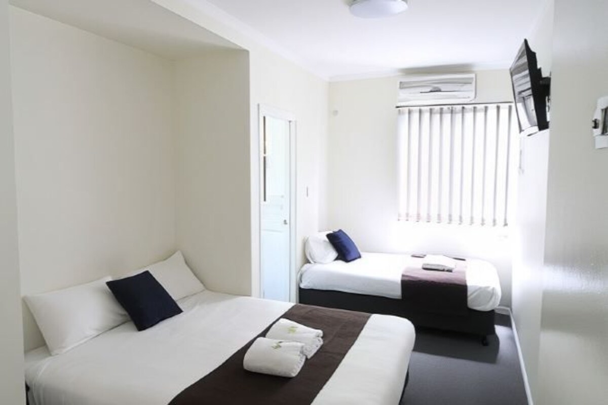 Une chambre d’hôtel avec deux lits, une fenêtre avec des stores, un appareil de climatisation et une porte.