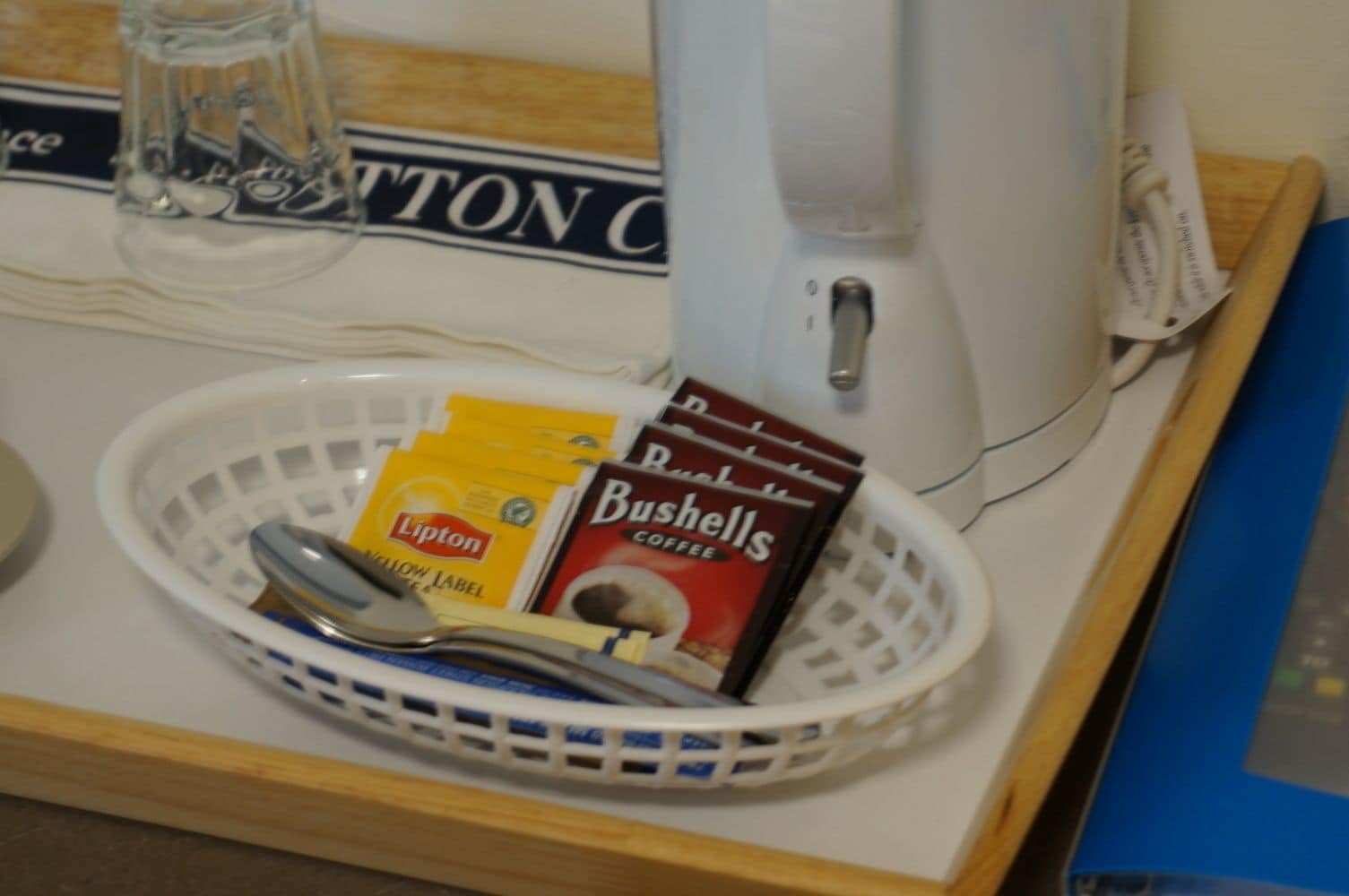 A coffee maker, a basket with coffee packets, and a spoon on a table.