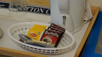 A coffee maker, a basket with coffee packets, and a spoon on a table.
