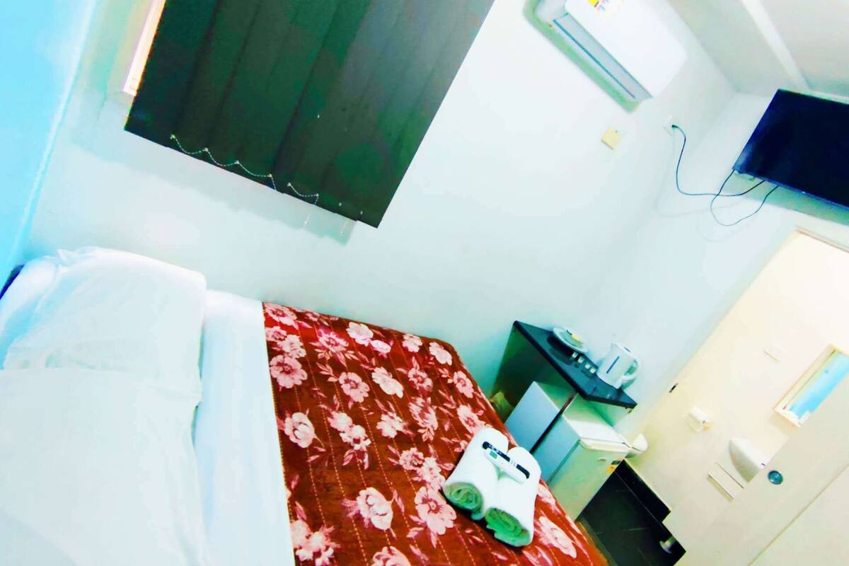 A hotel room with a bed, a desk, a chair, a television, and a door.
