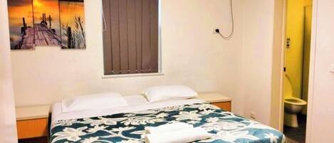 A bedroom with a bed, a window with blinds, an air conditioning unit, and a painting on the wall.