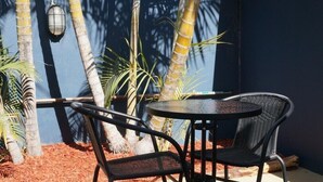 An outdoor patio with a round table and two chairs, surrounded by palm trees and a blue wall. - The Cliff House (Kangaroo Point)