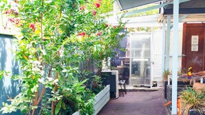 A covered walkway with a tiled floor, surrounded by planters with green plants and pink flowers. - The Cliff House (Kangaroo Point)