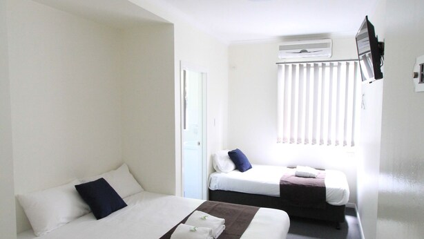 A hotel room with two beds, a window with blinds, an air conditioning unit, and a door. - The Cliff House (Kangaroo Point)