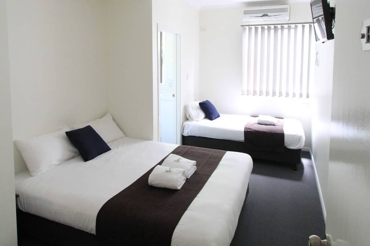 A hotel room with two beds, a window with blinds, an air conditioning unit, and a door.