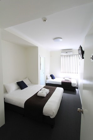 A hotel room with two beds, a window with blinds, an air conditioning unit, and a door.