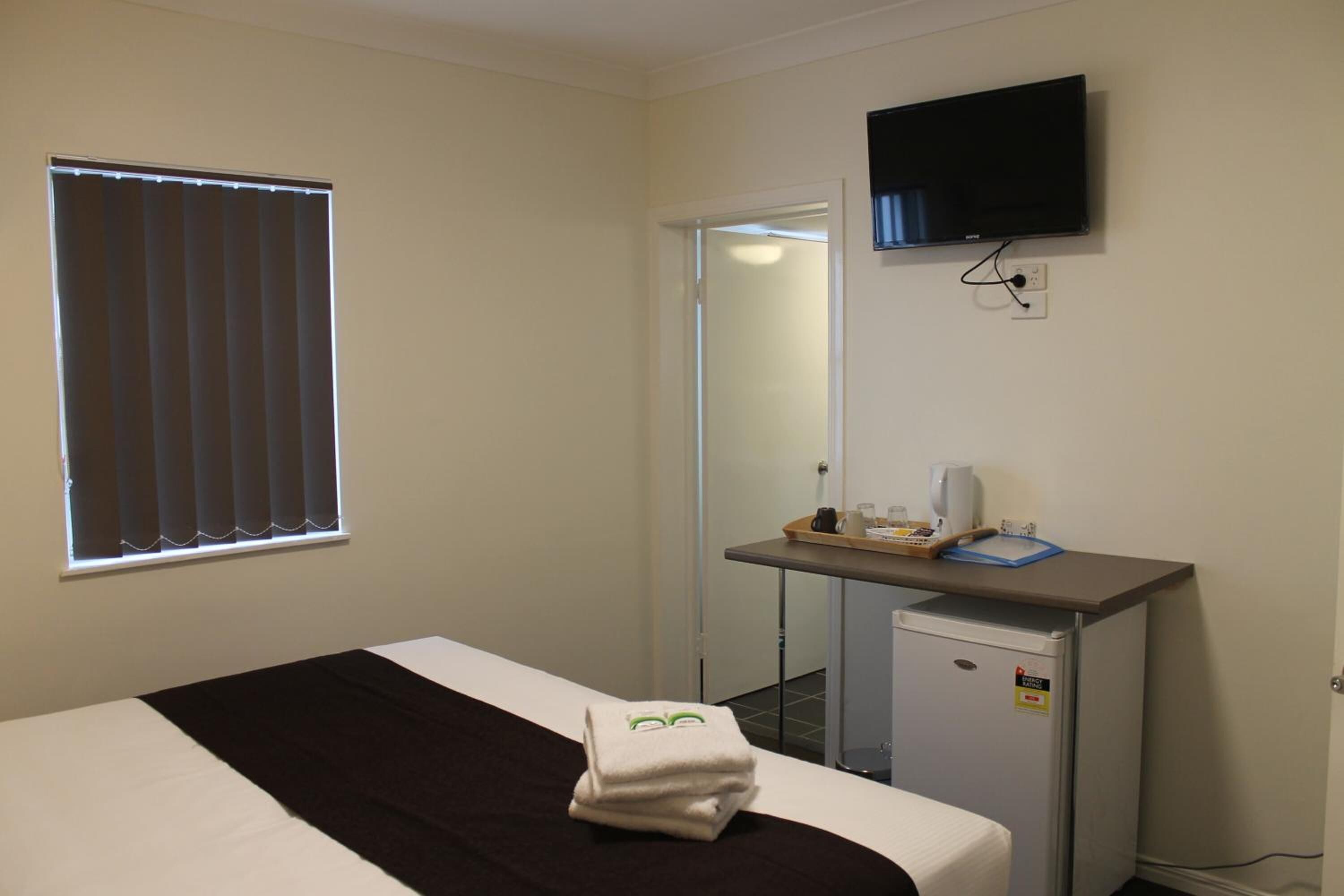 Ein Hotelzimmer mit Bett, Schreibtisch mit Computer, Fernseher und Fenster mit Jalousien.