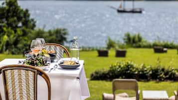 Mesa al aire libre con mariscos, copas de vino y una botella, con vista a un lago y follaje.