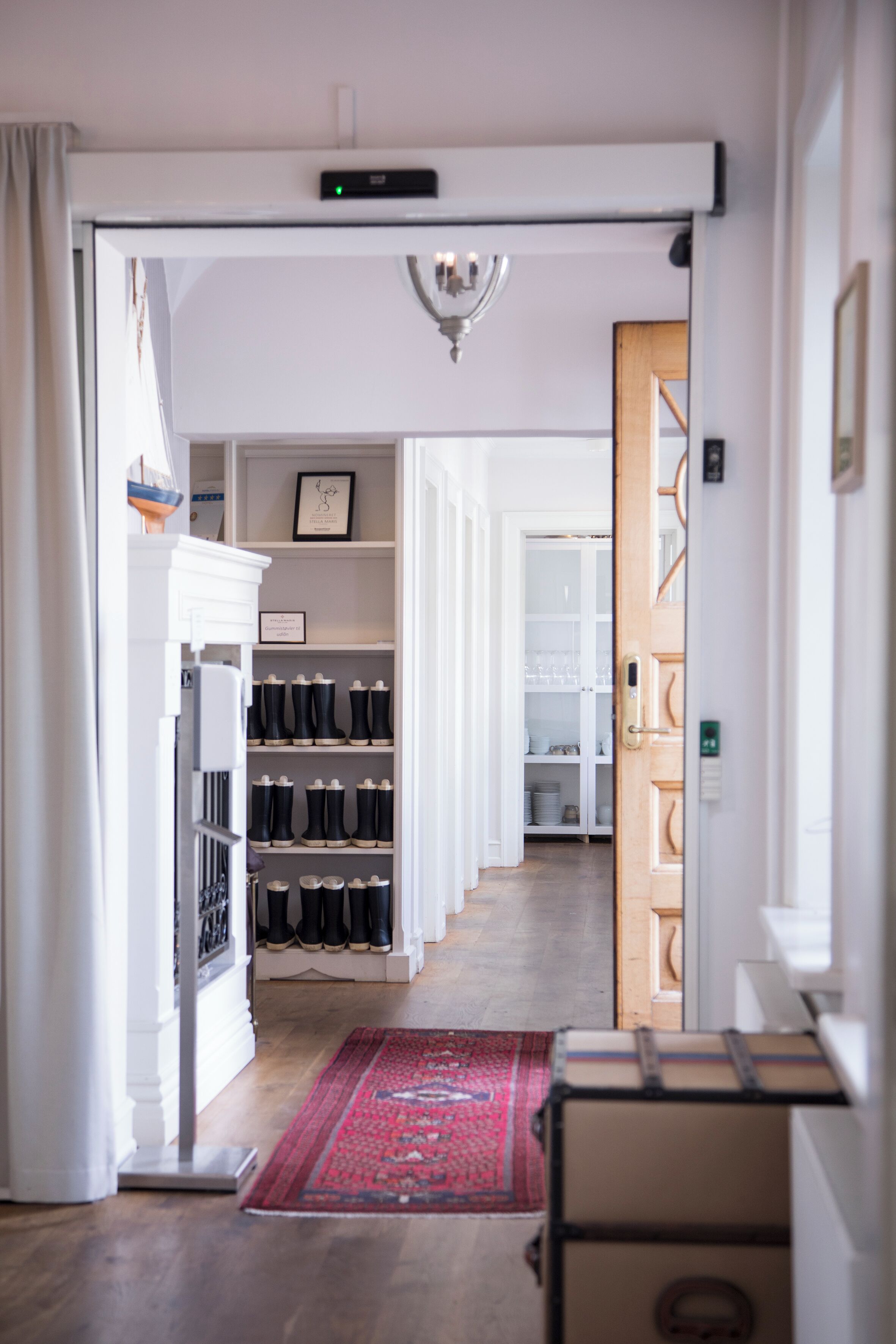 A hallway with a red rug, a wooden door, and a white closet with black boots.