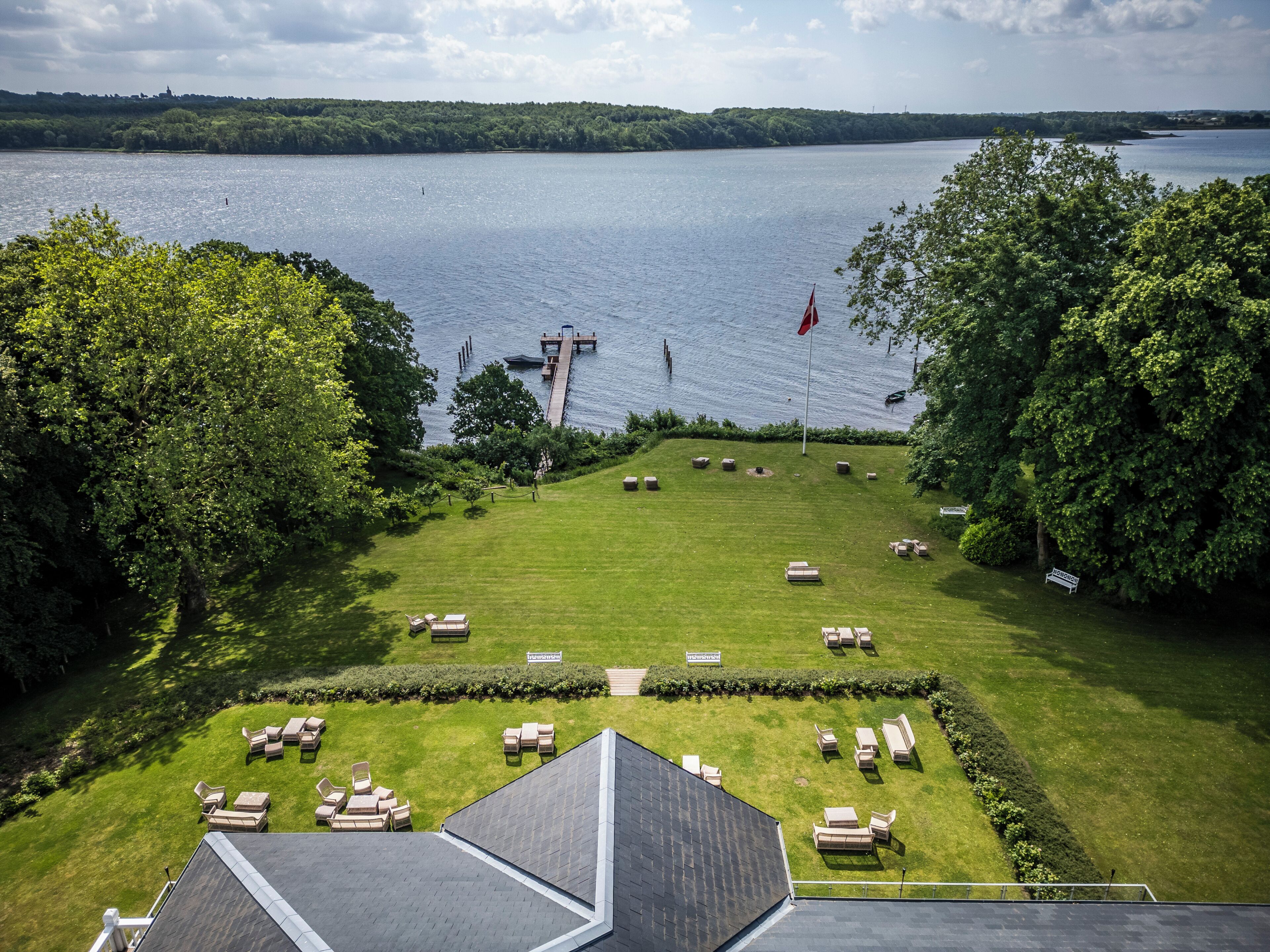 A lakeside property with a grassy lawn, outdoor seating, and a dock extending into the water.