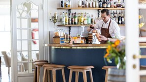 A bar area with wooden stools, shelves of bottles, and a bartender preparing drinks. - Stella Maris (Svendborg)