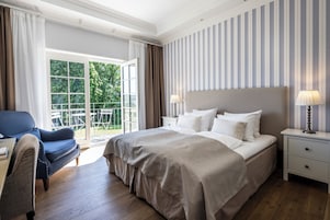 A hotel room with a large bed, a chair, a nightstand, and a view of the outdoors.