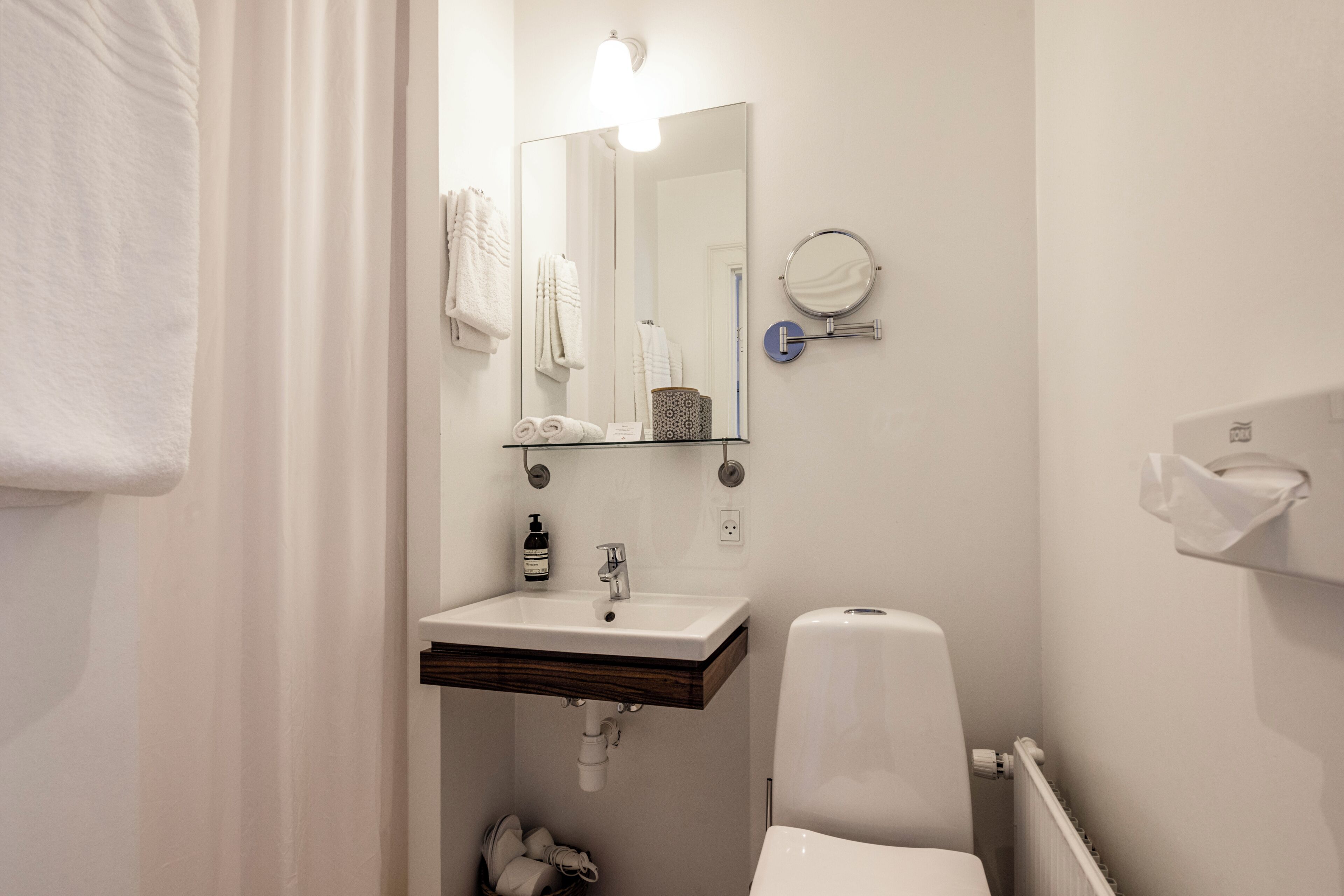 Un baño con un lavabo blanco, un espejo, un perchero para toallas, un inodoro y un secador de manos.