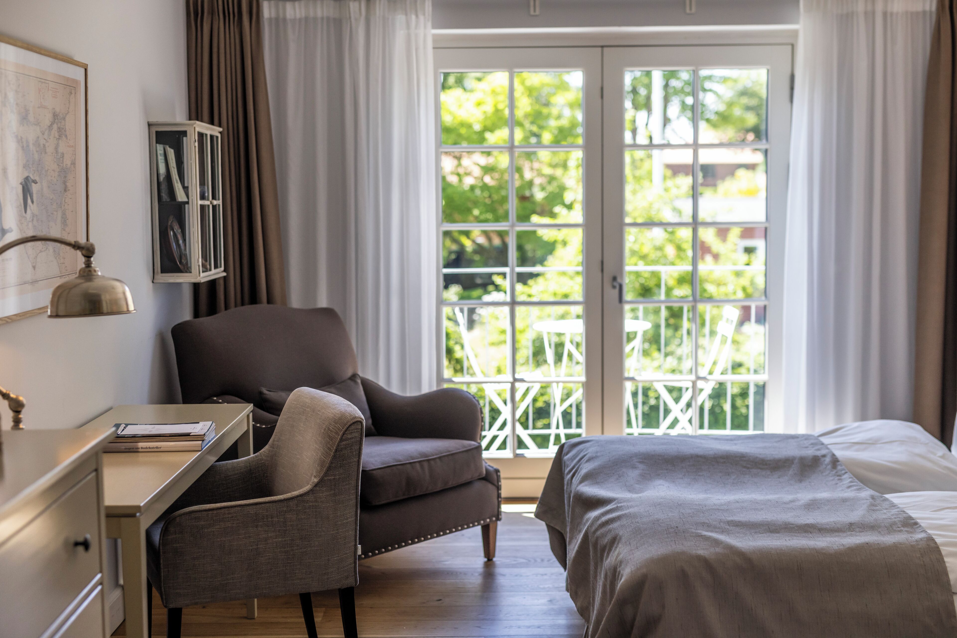A bedroom with a bed, a desk, a chair, and a window with a view of greenery.