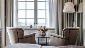 A hotel room with a bed, two armchairs, a small table with a vase of flowers, and a window with curtains. - Stella Maris (Svendborg)