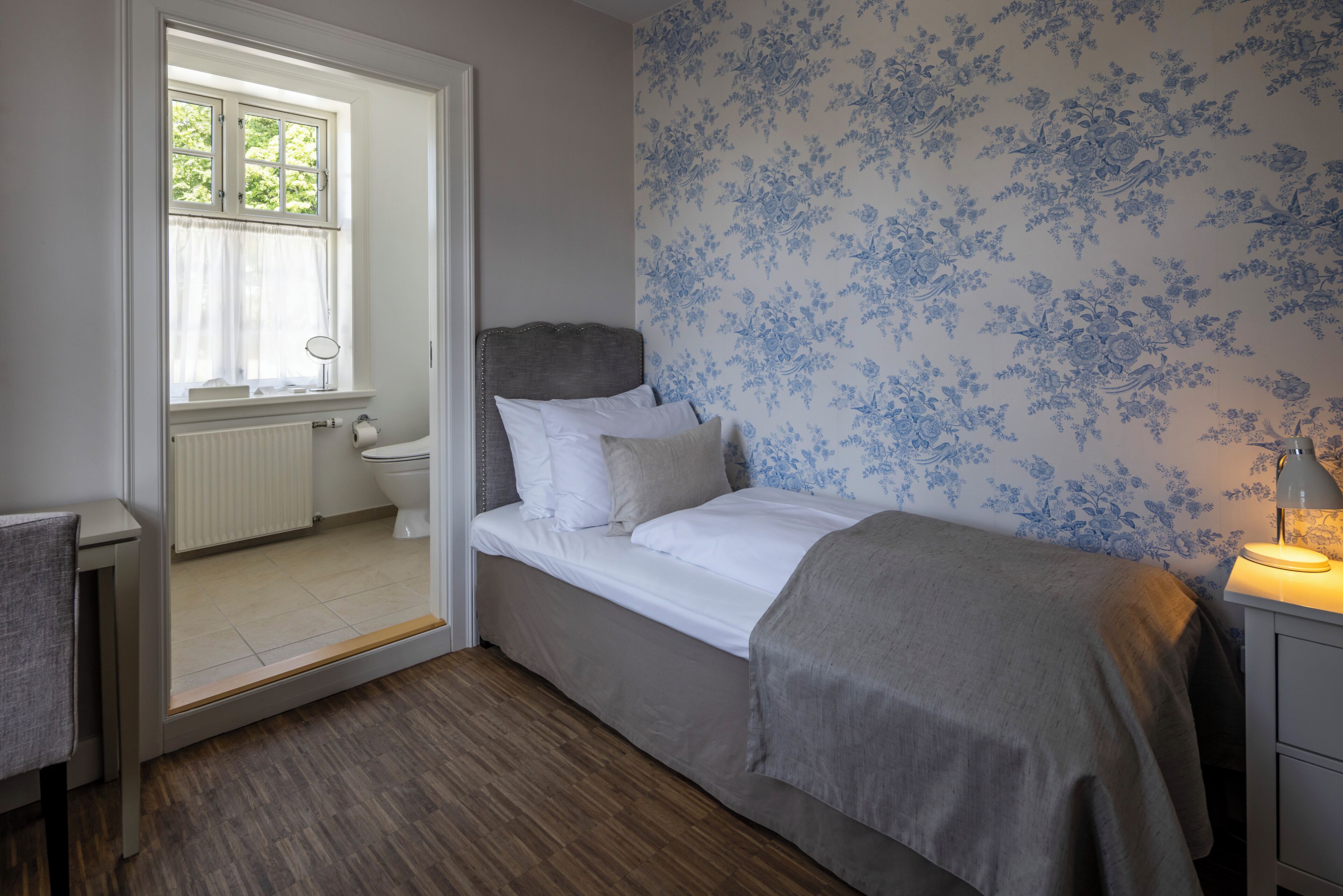 Une chambre à coucher avec un lit, une table de chevet avec une lampe, une fenêtre avec des rideaux et un radiateur.