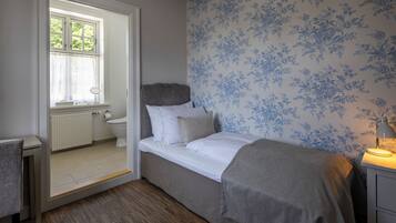 Une chambre à coucher avec un lit, une table de chevet avec une lampe, une fenêtre avec des rideaux et un radiateur.