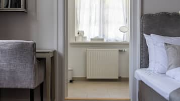Una habitación con cama, una silla, una ventana con cortinas, un radiador y una mesita.