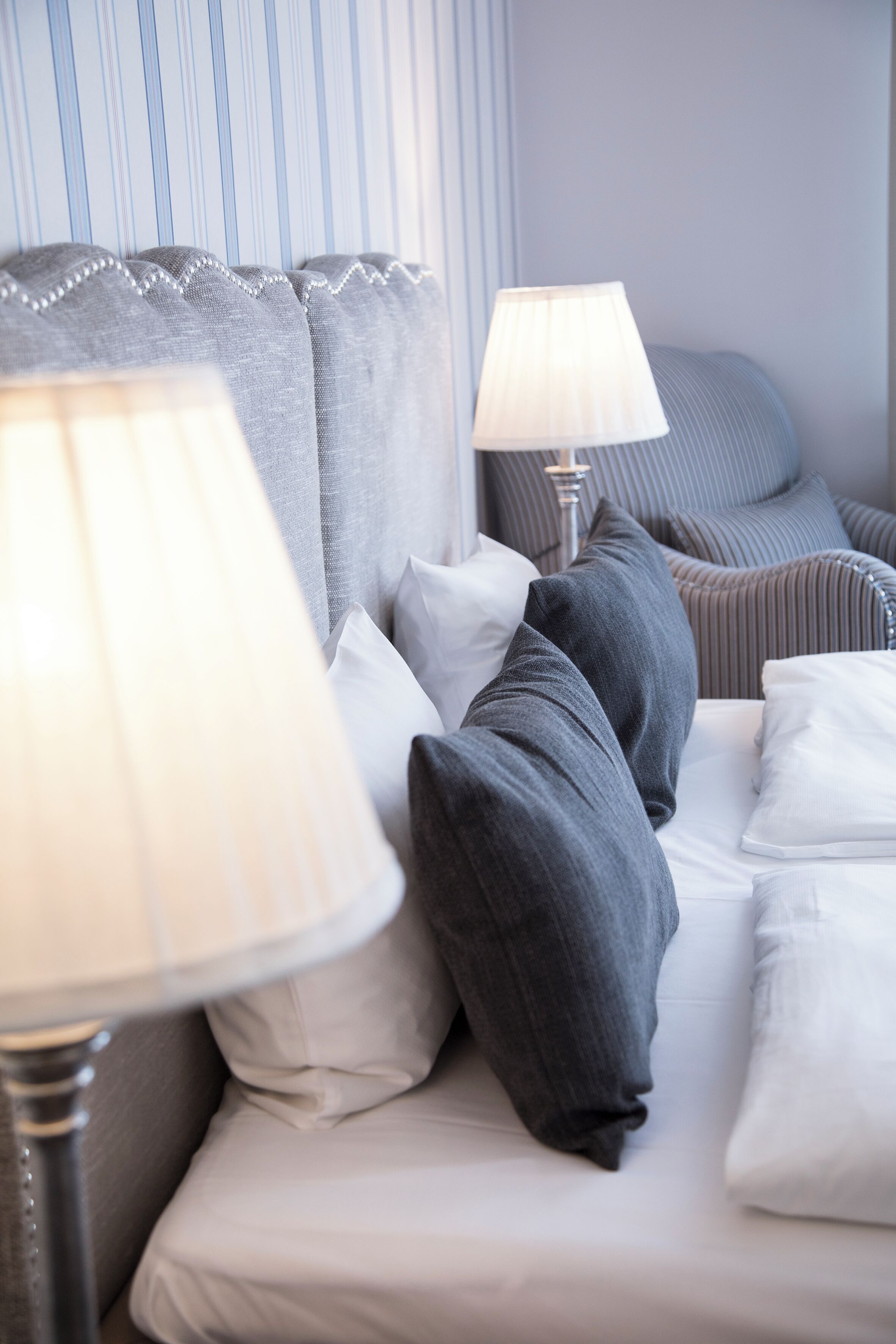 A neatly made bed with white and gray bedding, a striped headboard, and two bedside lamps.