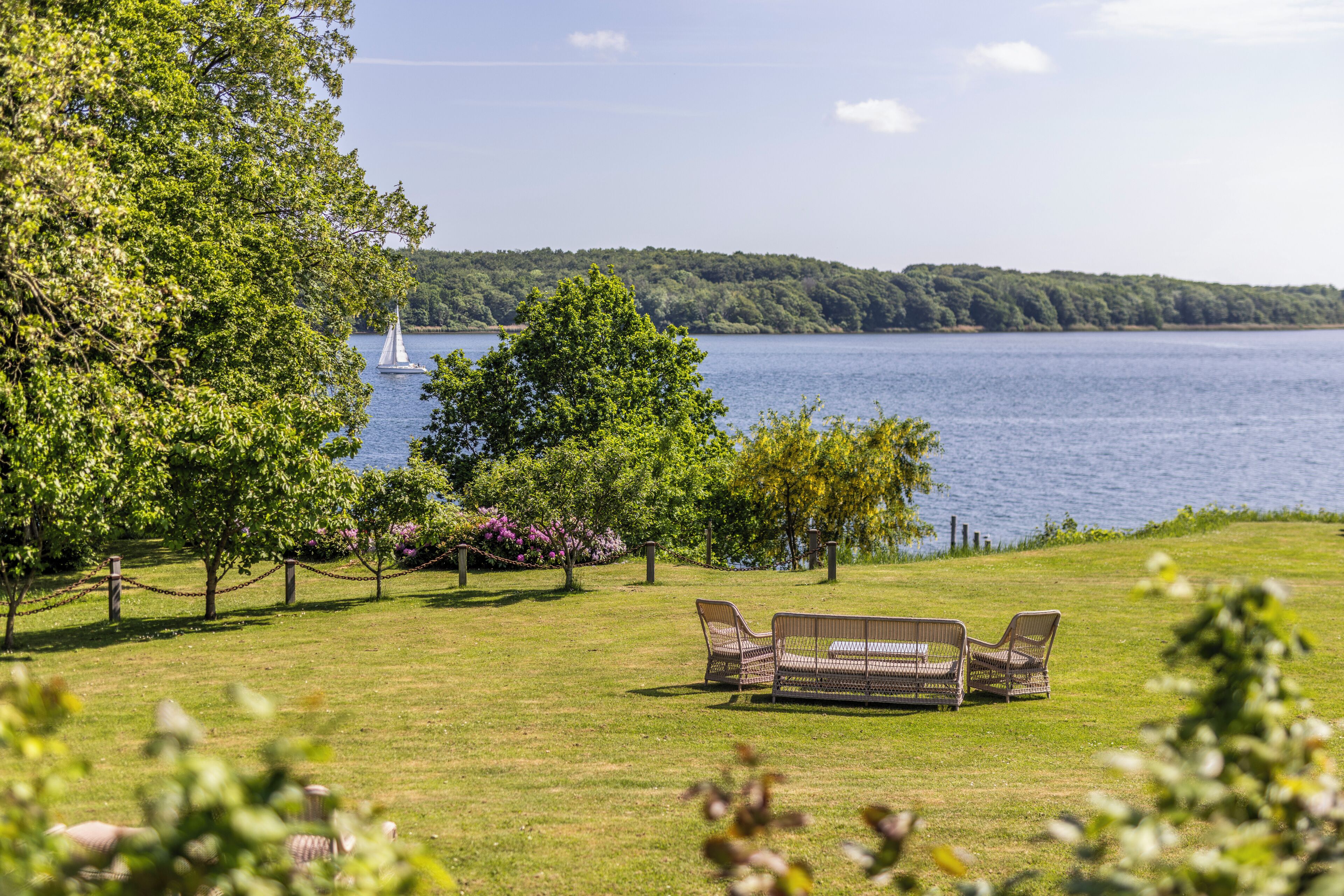 A grassy area with a seating arrangement overlooking a lake and a sailboat in the distance.