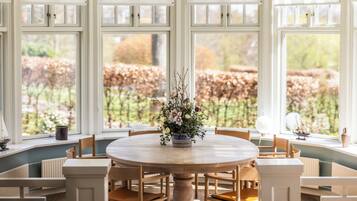 Un tavolo rotondo da pranzo con sedie, un vaso di fiori e vista su un giardino attraverso ampie finestre.