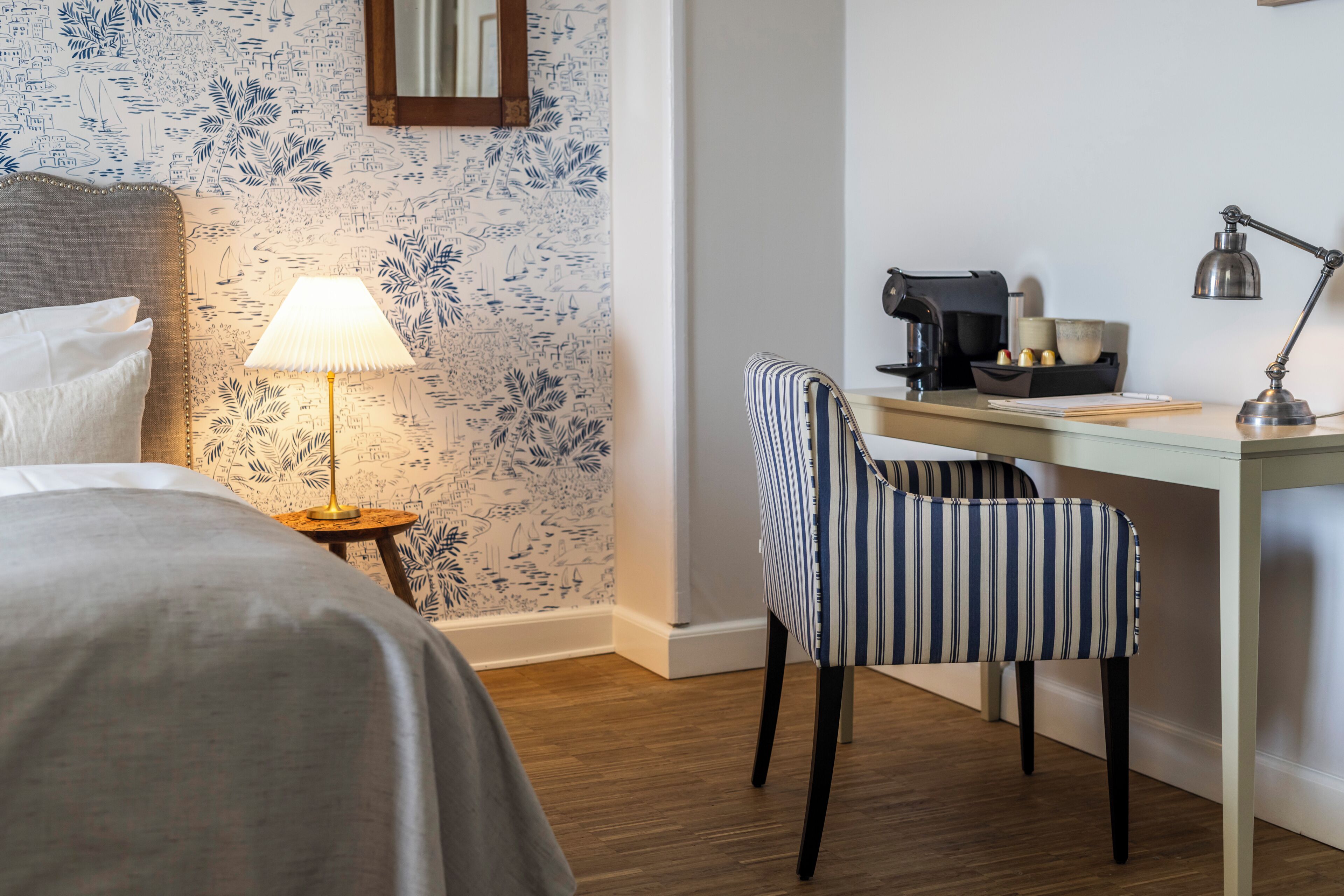 Una habitación de hotel con cama, escritorio, silla, lámpara y cafetera.