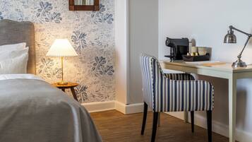 Una habitación de hotel con cama, escritorio, silla, lámpara y cafetera.