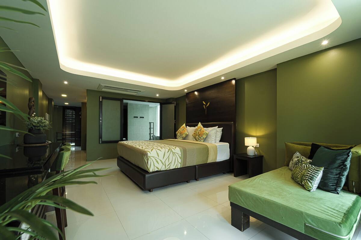 Une chambre moderne avec un grand lit, des tables de chevet, un canapé vert et une plante en pot.