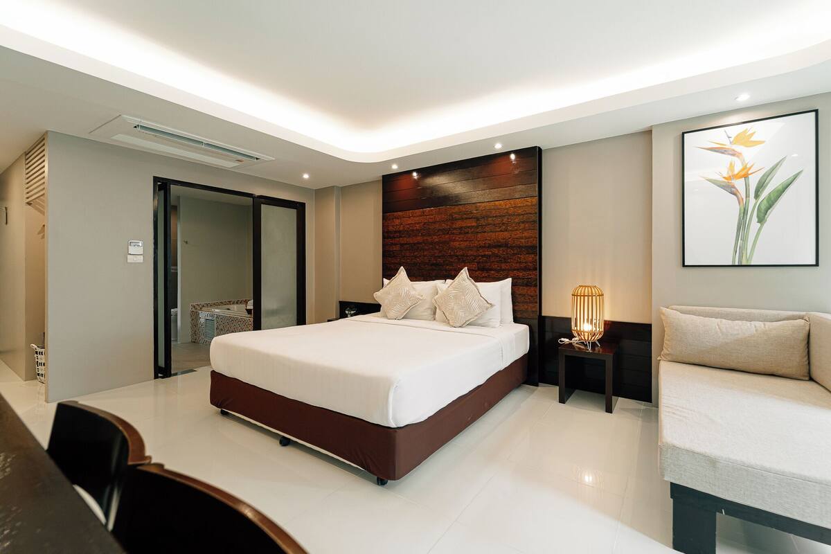 Une chambre d’hôtel moderne, dotée d’un grand lit, d’un canapé, d’un bureau et d’une salle de bain visible à travers une porte ouverte.