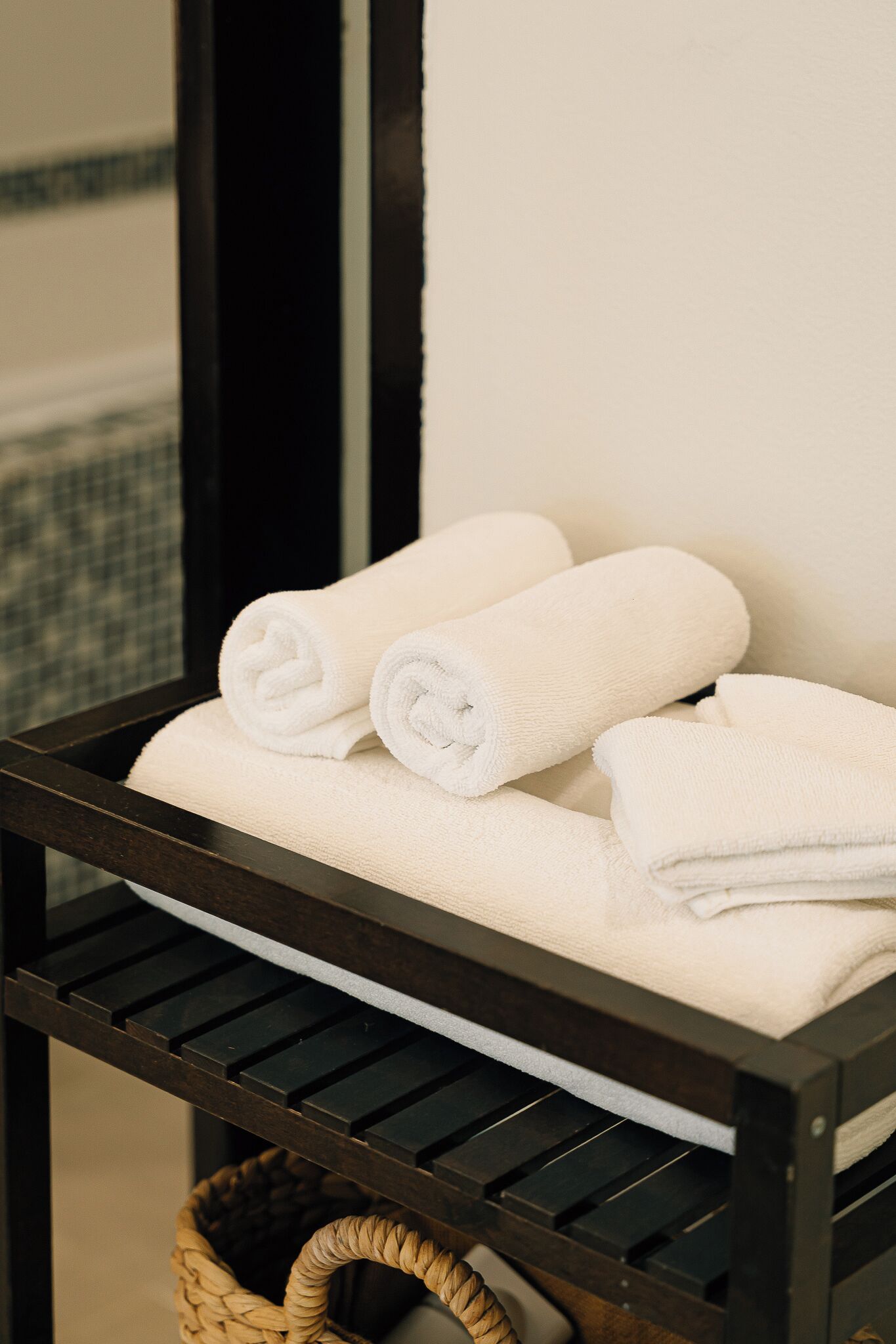 A wooden shelf with two rolled white towels and a wicker basket.