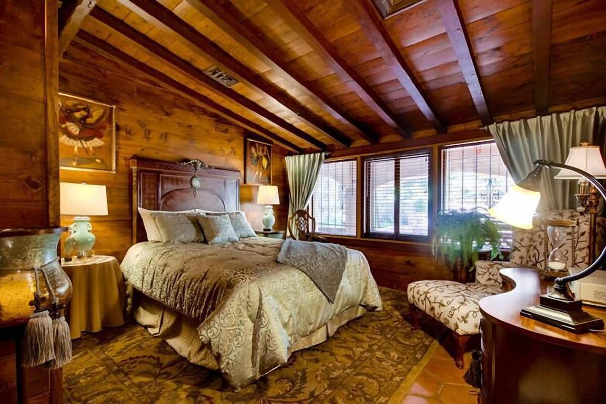 A cozy wooden room with a large bed, a small table, and a chair.