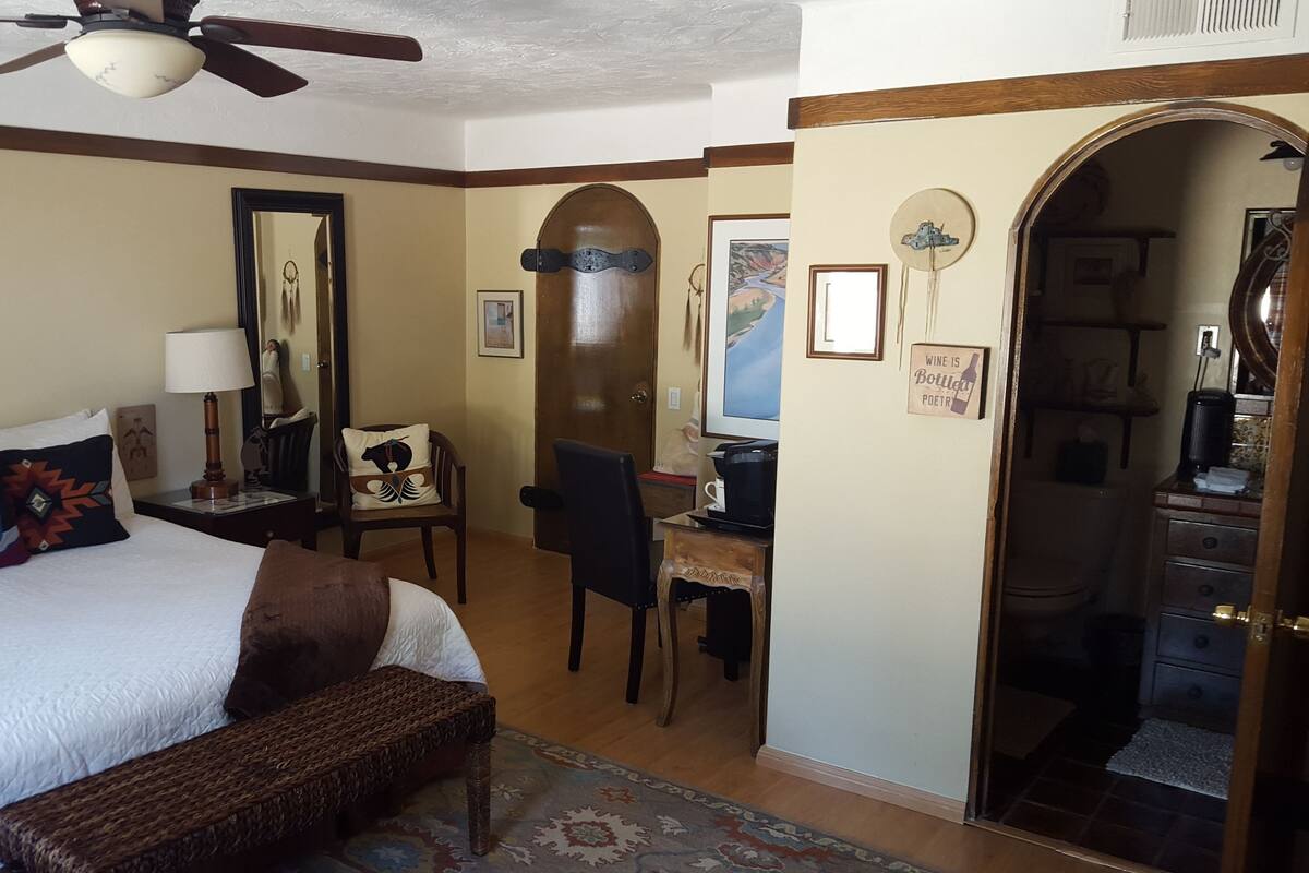 A hotel room with a bed, a desk, a chair, a mirror, and a wardrobe.