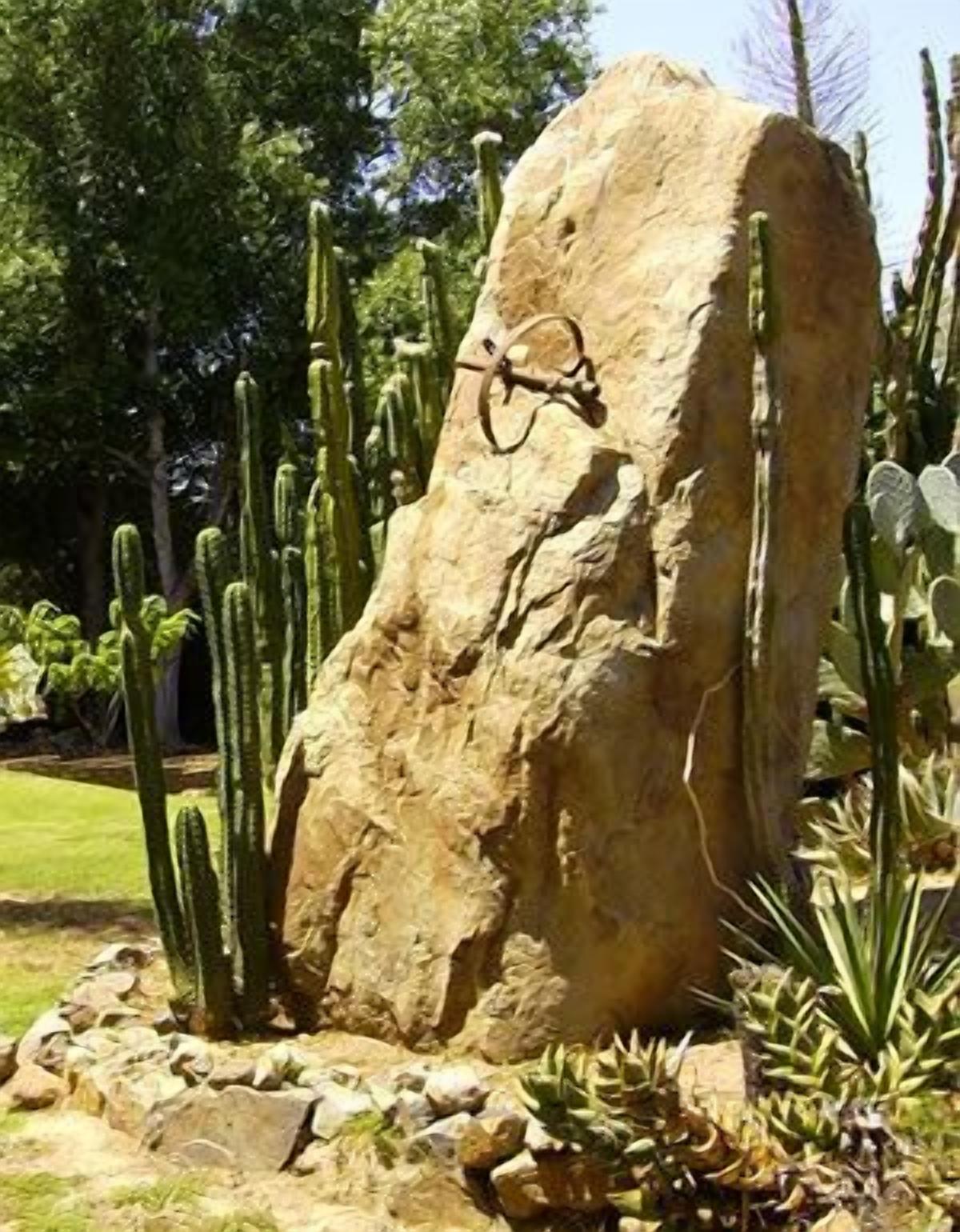 A large rock formation with a metal sculpture in a desert garden with cacti.